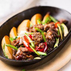 Grilled steak, baked potatoes and vegetables.  Beef meat stewed with potatoes, carrots, sweet red peppers, green onions and spices in frying pan on white wooden table.