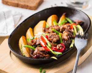 Grilled steak, baked potatoes and vegetables.  Beef meat stewed with potatoes, carrots, sweet red peppers, green onions and spices in frying pan on white wooden table.