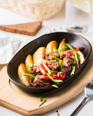 Grilled steak, baked potatoes and vegetables.  Beef meat stewed with potatoes, carrots, sweet red peppers, green onions and spices in frying pan on white wooden table.