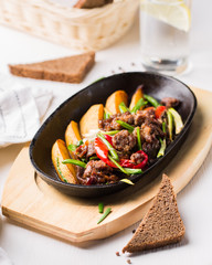 Grilled steak, baked potatoes and vegetables.  Beef meat stewed with potatoes, carrots, sweet red peppers, green onions and spices in frying pan on white wooden table.