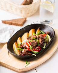 Grilled steak, baked potatoes and vegetables.  Beef meat stewed with potatoes, carrots, sweet red peppers, green onions and spices in frying pan on white wooden table.
