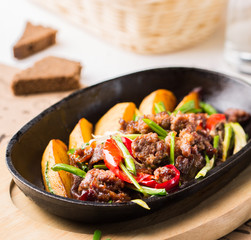 Grilled steak, baked potatoes and vegetables.  Beef meat stewed with potatoes, carrots, sweet red peppers, green onions and spices in frying pan on white wooden table.