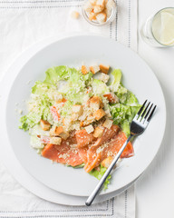 Leaf vegetable salad with smoked salmon, parmesan cheese and bread crumbs in a white plate on a light wooden background. View with copy space. Flat lay, top view