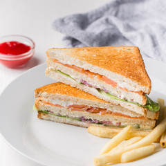 Freshly made club sandwiches with French fries served on white plate. Pressed double toasts with leaf vegetable salad, smoked salmon and cheese served on paper on a wooden table. Street fast food.