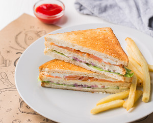 Freshly made club sandwiches with French fries served on white plate. Pressed double toasts with leaf vegetable salad, smoked salmon and cheese served on paper on a wooden table. Street fast food.