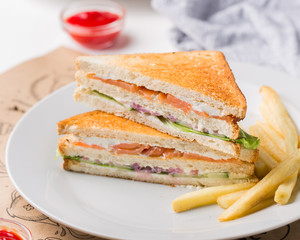 Freshly made club sandwiches with French fries served on white plate. Pressed double toasts with leaf vegetable salad, smoked salmon and cheese served on paper on a wooden table. Street fast food.