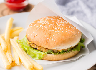 Fresh tasty burger and french fries served on white plate. Delicious burger with beef, tomato, cheese and lettuce served on paper on a wooden table. Street fast food