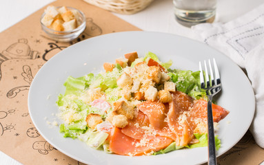 Leaf vegetable salad with smoked salmon, parmesan cheese and bread crumbs in a white plate on a light wooden background. View with copy space. Flat lay, top view