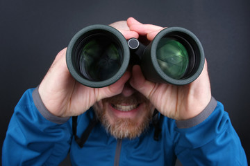 bearded man looking through binoculars on grey background.