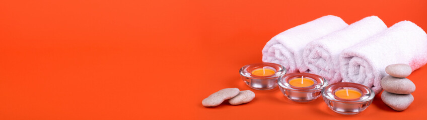 Fototapeta na wymiar Towels, candles for a spa relaxation on orange background. Banner.