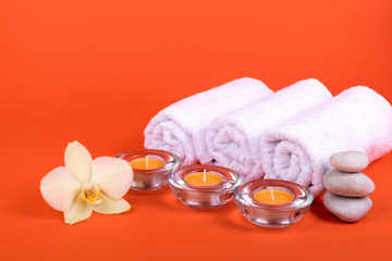 Obraz na płótnie Canvas Towels, candles and orchid flowers for a spa relaxation on orange background