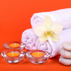 Towels, candles and orchid flowers for a spa relaxation on orange background.