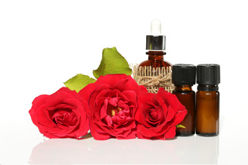 Obraz na płótnie Canvas oil roses set. rose essential oil in brown glass bottles and bright red roses on a white background. Pure Organic Rose Oil
