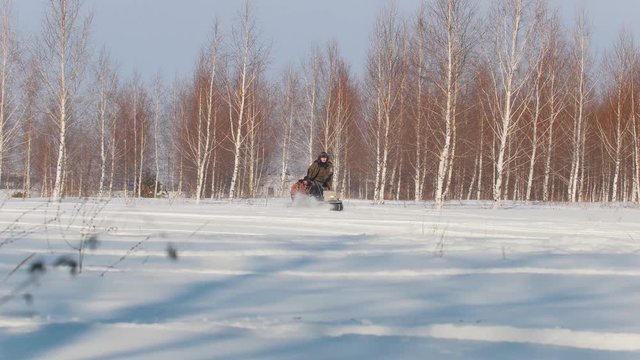 Man in winter clothes fast riding, maneuvering and carrying passenger in the trailer of mini snowmobile through snowdrifts