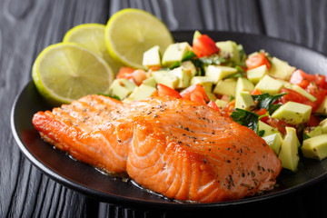 Freshly cooked salmon steak with lime, avocado and tomatoes close-up on a plate. horizontal