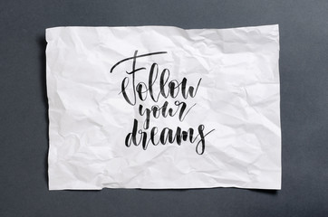 Follow your dreams. Handwritten text on white crumpled paper. Inspirational quote.