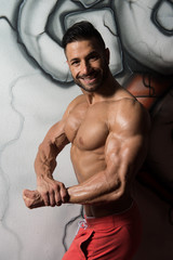 Fototapeta na wymiar Muscular Man Flexing Muscles At Graffiti Wall