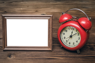 Photo frame with copy space and retro style red alarm clock on wooden table background.