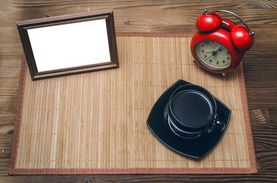 Blank photo frame with copy space, cup of black coffee and red alarm clock on office table background. Coffee break.