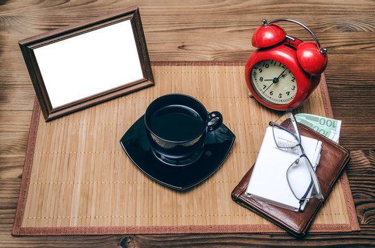 Photo frame with copy space, red alarm clock and cup of black coffee and wallet with money on office desk table background. Coffee break.