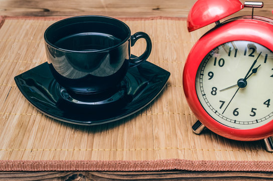 Red alarm clock and cup of black coffee on office desk table background. Coffee break concept.