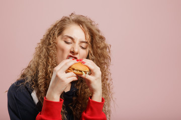 Beautiful young girl with burger curly hair on pink background. Concept fast food, snack