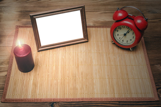 Photo frame with copy space, red alarm clock and burning candle on wooden desk table background with copy space.