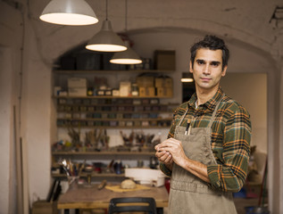 Handsome young man in pottery workshop holding clay