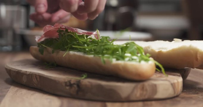 Slow motion man hands put coppa on baguette on wood board