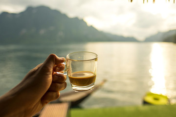 hand holding coffee glass in good morning time with blur lake and mountain background