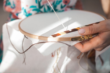 Young beautiful woman is engaged in embroidering a dagger on the embroidery frame in a colored...