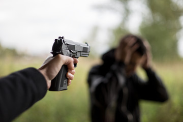 Give me chance. Shocked frightened man with his hands tied while a killer standing near him and holding a gun