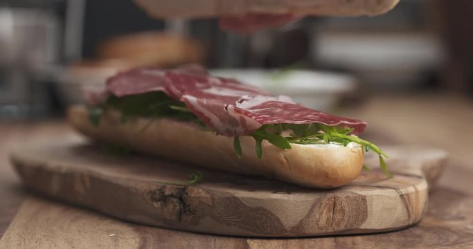 Slow motion man hands put top on coppa baguette on wood board