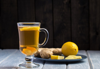 A cup of ginger tea with lemon on a wooden background.