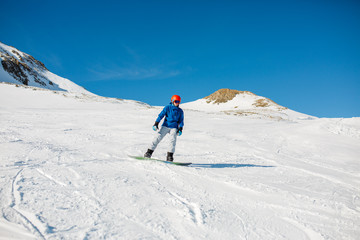 Image of sports man wearing blue jacket, helmet with snowboard riding on snowy slope