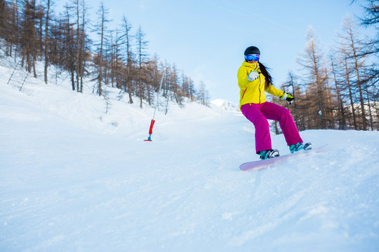Photo of female athlete wearing helmet and mask snowboarding from snowy slope with trees