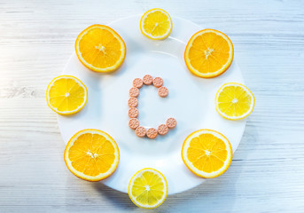 Vitamin C concept. Orange slices and citrus fruits shape pills on a white plate.