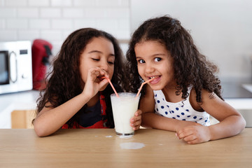 Little girls sharing a glass of milk at kitchen counter