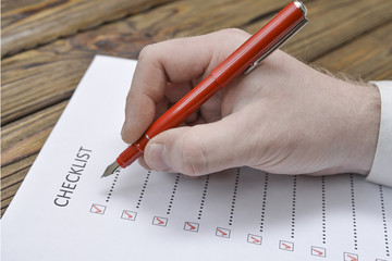 hand of businessman with pen writes on checklist