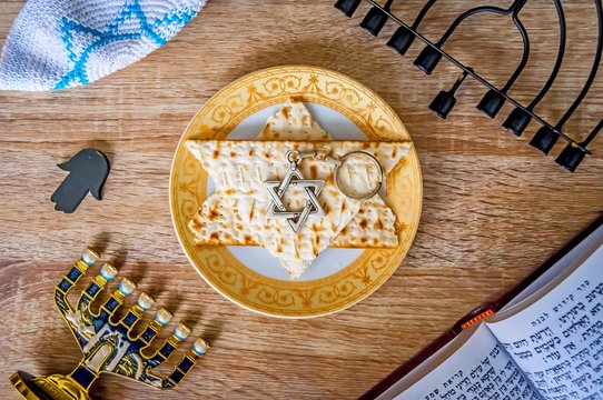 Jewish tradition and Judaism concept stock image. Hebrew prayer book, matzah pieces on a plate, Jewish "kippah" cap, David star hexagram, Hanukkah candle stand and other symbols.