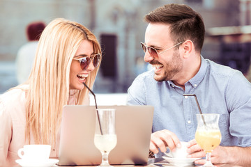 Happy young man and woman using laptop in the city.