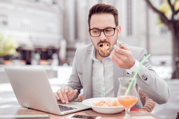 Young man eats pasta  and looks in the monitor.