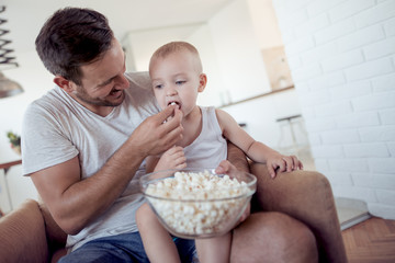 Happy father and little son with popcorn at home