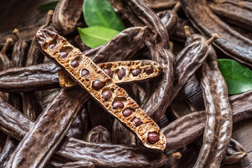 Carob pods and carob beans on the wooden table. - obrazy, fototapety, plakaty