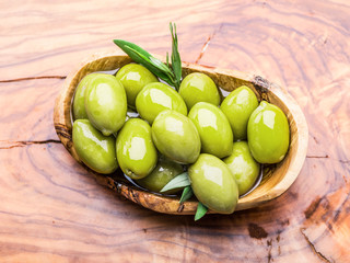 Whole table olives in the wooden bowl on the table.