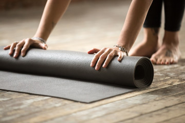 Hands of attractive young woman unfolding black yoga or fitness mat before working out at home in...