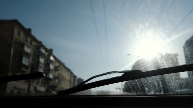 View from the car to the city. Focus on the dirty windshield. The car is in motion.