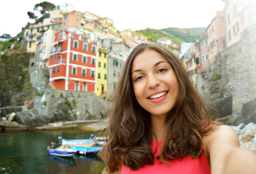 Selfie woman taking self portrait with typical italian village on the background. Girl holding smartphone camera to take a picture of herself in her summer vacations at Riomaggiore, Five Lands, Italy