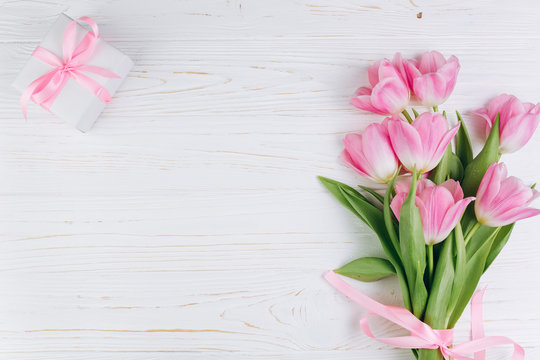 Pink tulips and gift on a white wooden background, copy space and flat lay. Mother's Day concept.