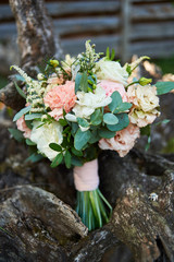 Obraz na płótnie Canvas Beautiful wedding bouquet of fresh white and pink roses, blue flowers and greenery standing on wood stump outdoors, free space. Bridal bouquet, close up